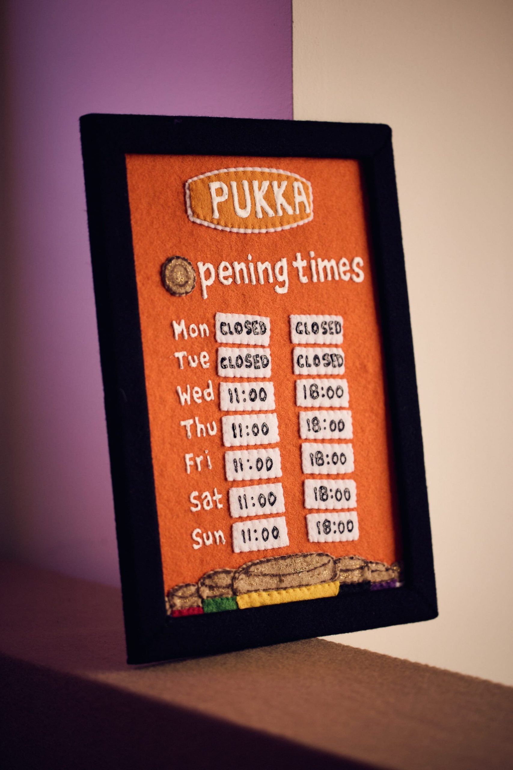 a sign made of felt showing opening times for an art installation