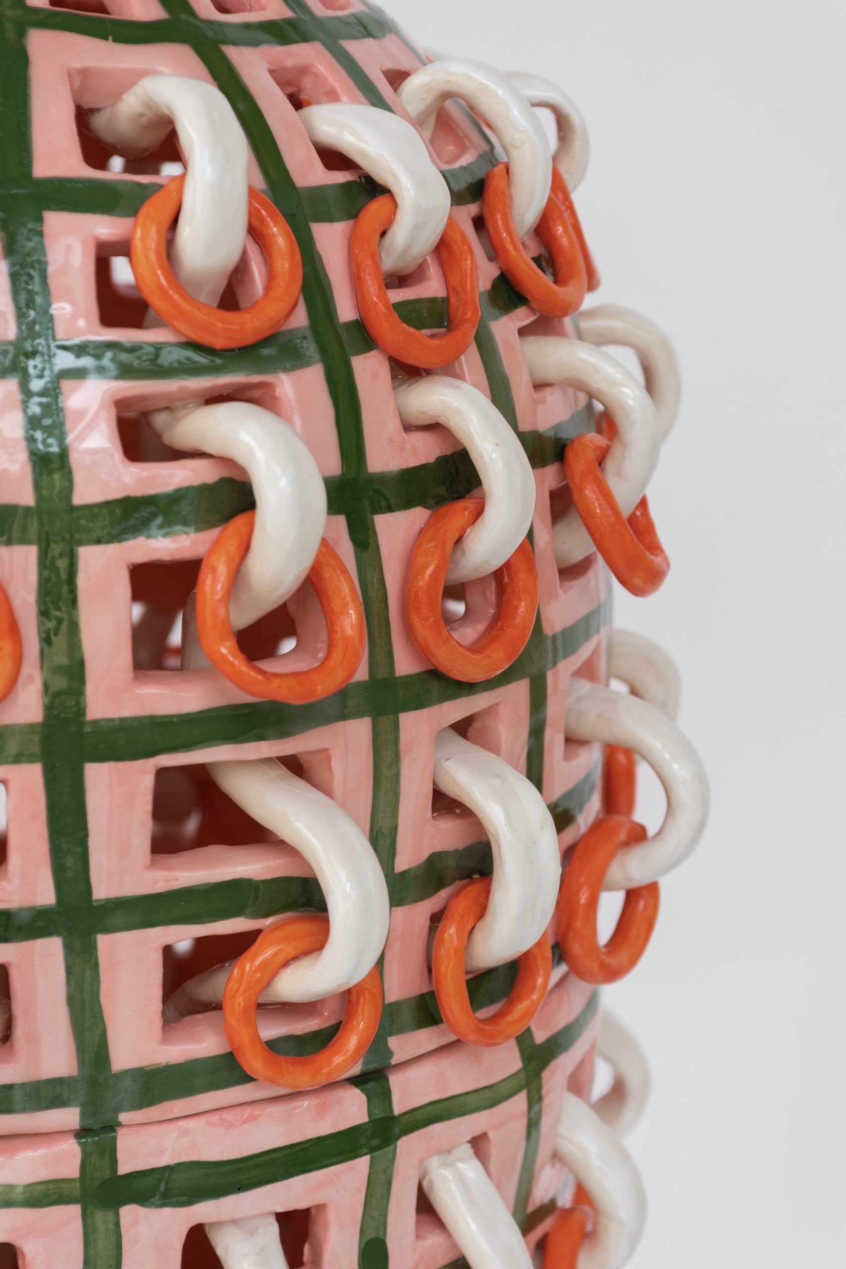 a detail of a ceramic sculpture showing white rings in the surface, with orange rings hanging off of those